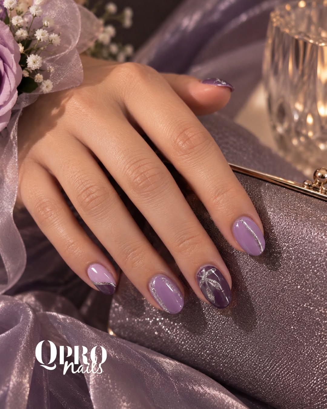 Lilac and plum nails with silver glitter lines beside a shimmering clutch