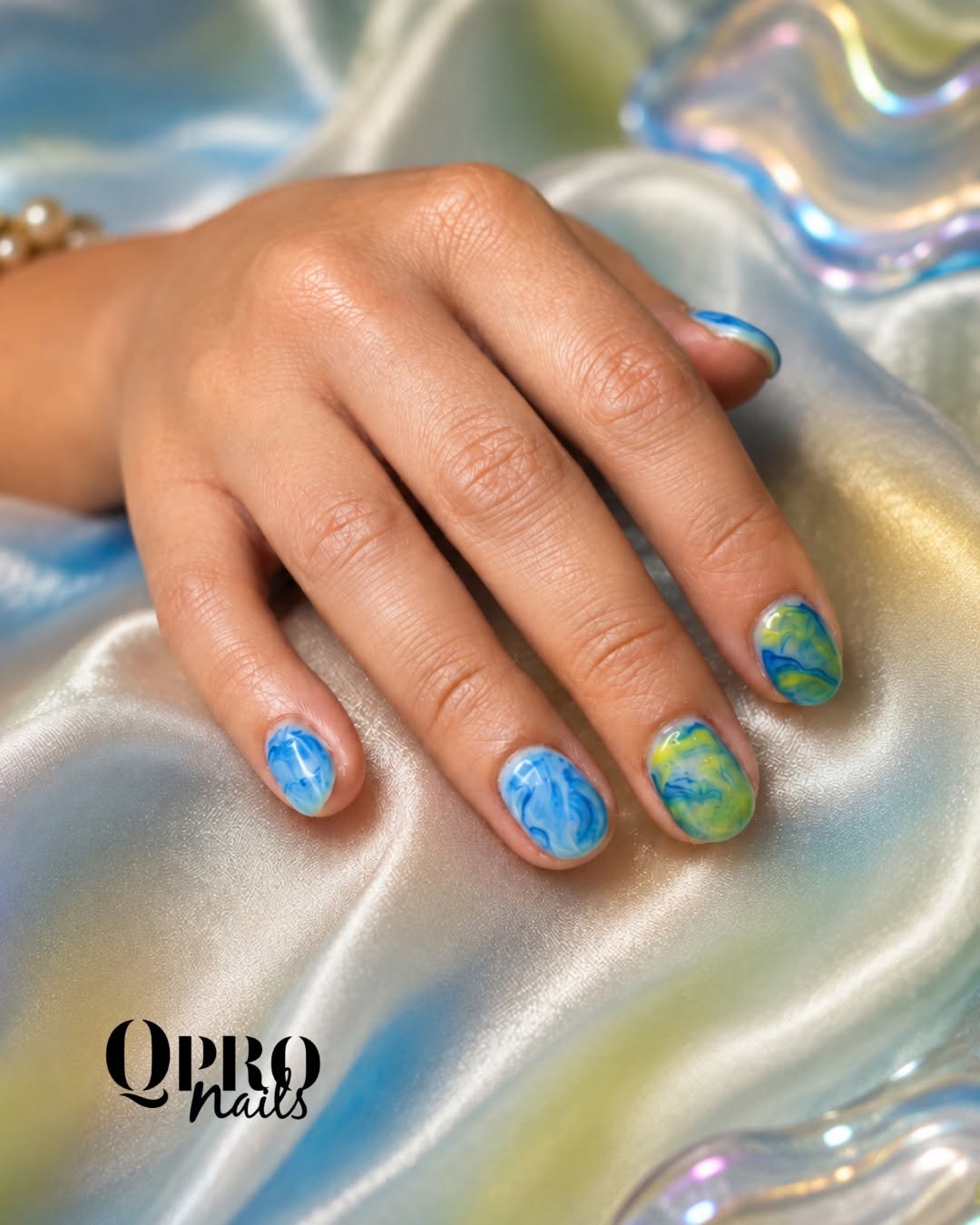Short nails with blue and green marbled swirls on iridescent satin